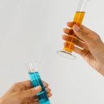 Close-up of hands holding graduated cylinders with blue and orange liquids, symbolizing scientific research.