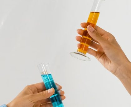 Close-up of hands holding graduated cylinders with blue and orange liquids, symbolizing scientific research.