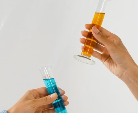 Close-up of hands holding graduated cylinders with blue and orange liquids, symbolizing scientific research.